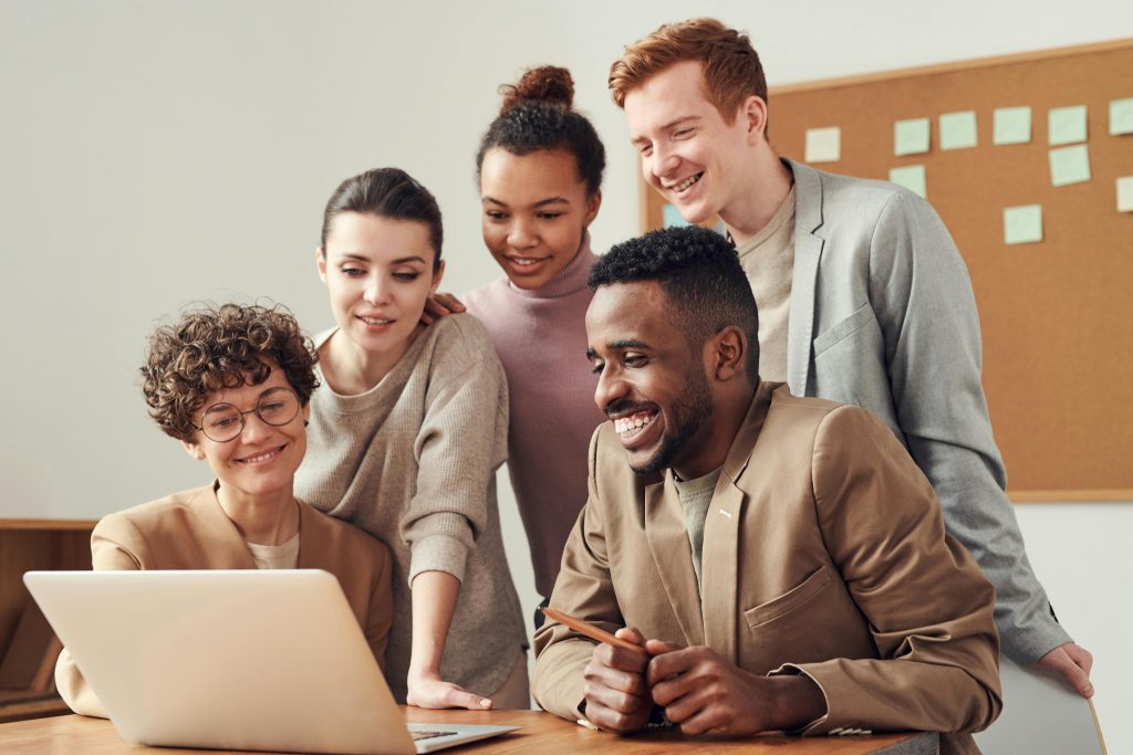Young coworkers in a diverse workplace look at a laptop smiling